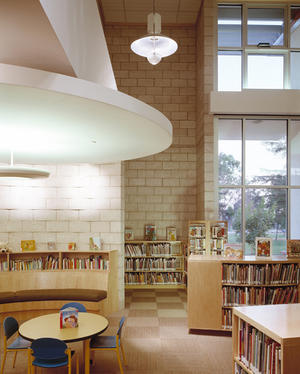 In this photo, a lowered ceiling, a small-scaled arc of bench, and a bookshelf make the children’s story amphitheatre. - Photo Credit: RMA Photography, Inc.