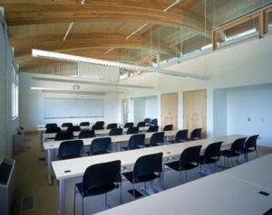 The classroom shown in this photograph is located on the second floor. Large exterior and interior windows for daylighting combine with daylight-sensing fixtures to ensure ample lighting. FSC-certified wood can be seen in the ceiling and doors. Desks, chairs, and carpeting are made of recycled materials. Low- or no-VOC materials combine with natural ventilation to provide a healthy indoor environment. - Photo Credit: Robb Williamson