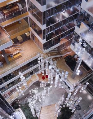 The natural light enhancement system utilizes a series of roof-mounted heliostats (mirrors) that track the sun's movement across the skylight to fixed mirrors. The fixed mirrors further reflect the light to a series of prismatic louvers located at the top of the atrium. The louvers also move with the sun’s path and elevation and reflect glaring, direct sunlight back to the mirrors, allowing diffuse light to enter the atrium. Once in the atrium, the light is further reflected to the floors by a system of hanging prismatic mobiles, shown in this photograph, reflective panels, and a reflective light wall on the inner surface of the atrium. - Photo Credit: Roland Halbe