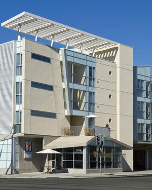 This photograph shows the facade facing a street intersection, retail space at street level, and a rooftop garden trellis. - Photo Credit: Bernard Andre Photography
